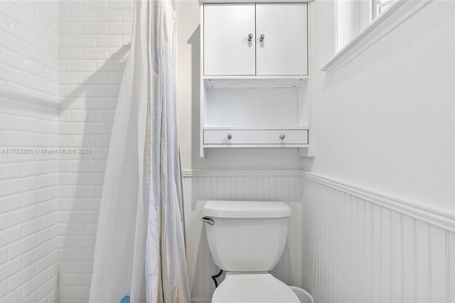 bathroom featuring curtained shower, wainscoting, and toilet