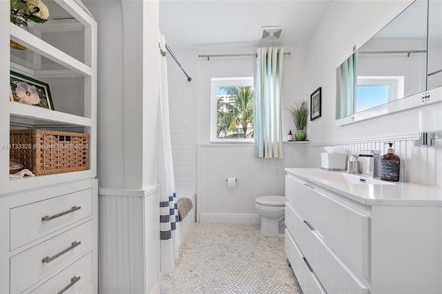 bathroom with toilet, a wainscoted wall, shower / bathtub combination with curtain, tile patterned flooring, and vanity