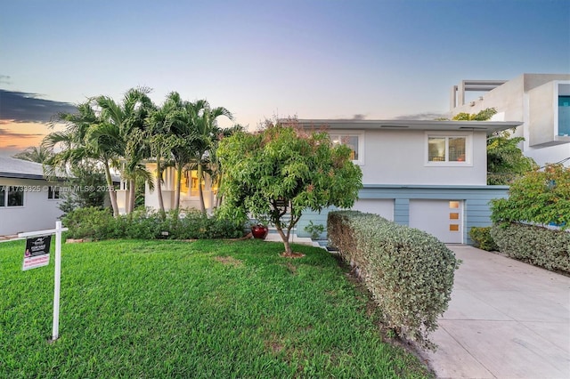 view of front facade featuring a garage, concrete driveway, a front yard, and stucco siding