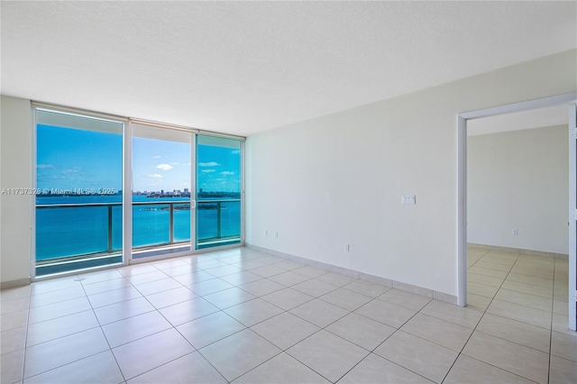 empty room with a textured ceiling, a wall of windows, and light tile patterned flooring