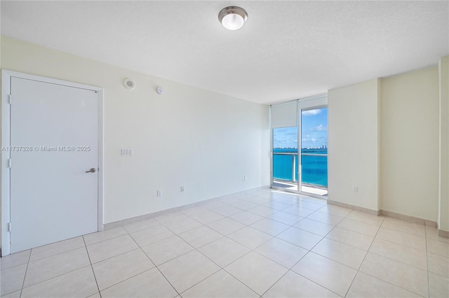 tiled spare room featuring a textured ceiling, floor to ceiling windows, and a water view