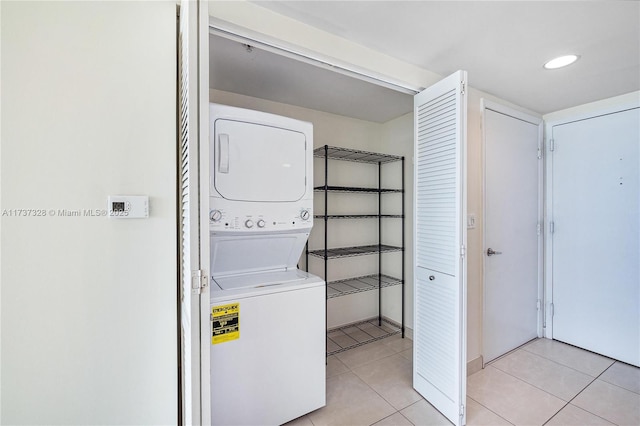 clothes washing area featuring light tile patterned flooring and stacked washer and clothes dryer