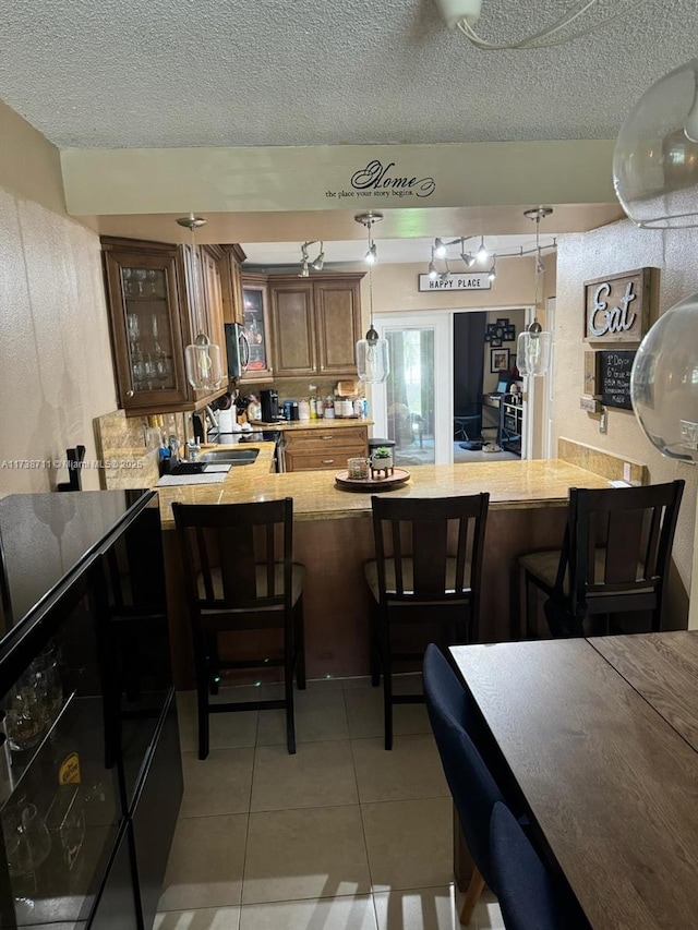 kitchen featuring kitchen peninsula, hanging light fixtures, a textured ceiling, and light tile patterned floors