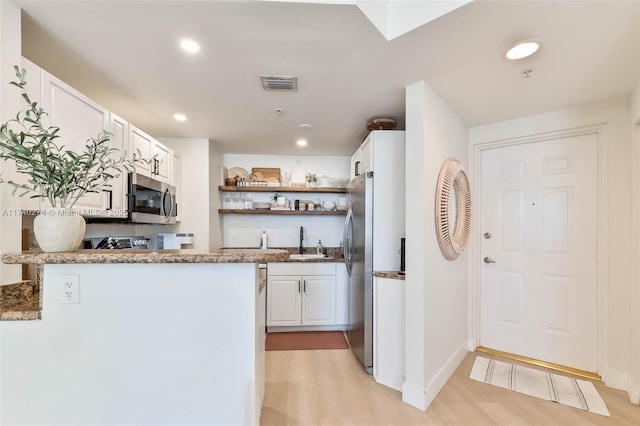 kitchen featuring sink, stainless steel appliances, white cabinets, kitchen peninsula, and light wood-type flooring