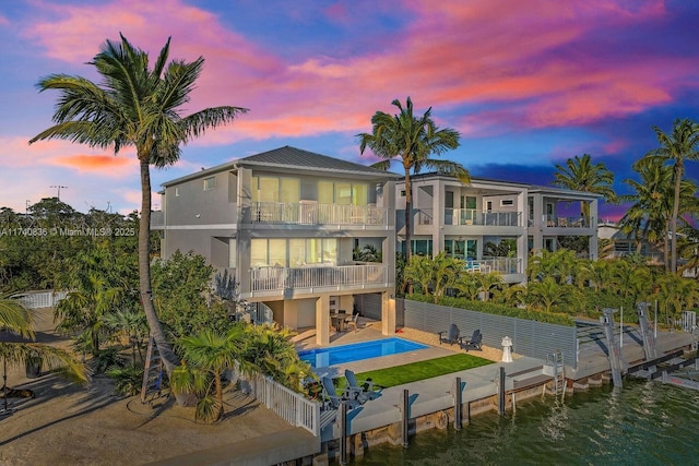 back house at dusk with a patio area, a balcony, and a water view