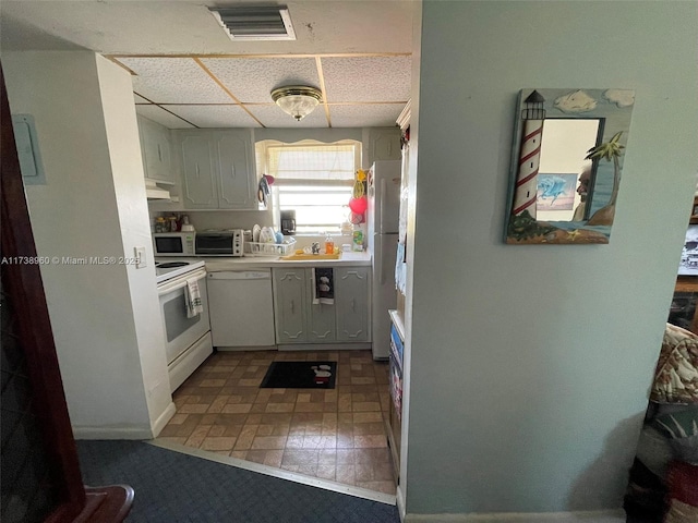 kitchen with a drop ceiling, white appliances, and white cabinetry