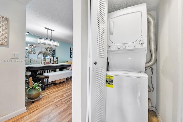 laundry room with stacked washer and dryer, wood-type flooring, and a textured ceiling