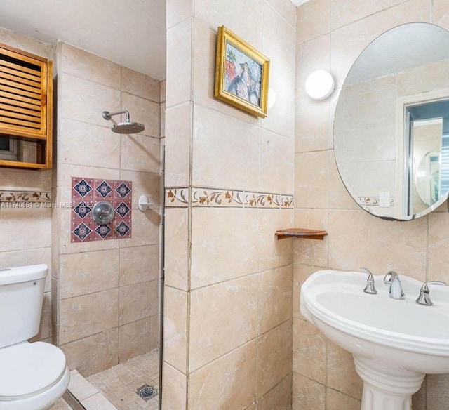 bathroom with tiled shower, toilet, sink, and tile walls