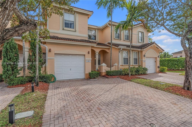 view of front facade with a garage, a tiled roof, decorative driveway, and stucco siding