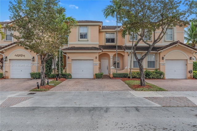 multi unit property featuring a garage, a tiled roof, decorative driveway, and stucco siding