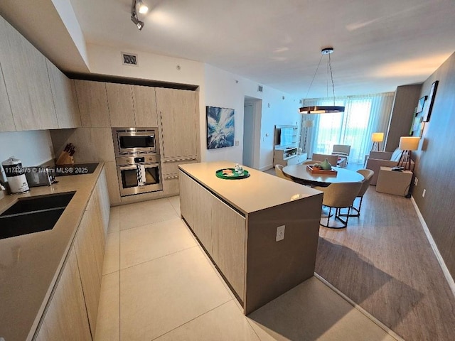 kitchen featuring sink, decorative light fixtures, a center island, light brown cabinets, and stainless steel appliances