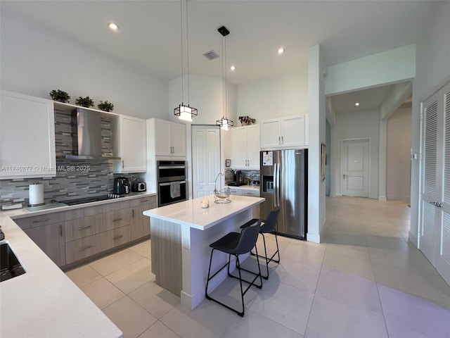 kitchen with a kitchen island, appliances with stainless steel finishes, pendant lighting, white cabinets, and wall chimney exhaust hood