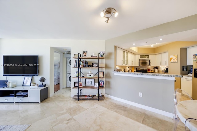 interior space with white cabinetry, light stone countertops, stacked washer and clothes dryer, and appliances with stainless steel finishes