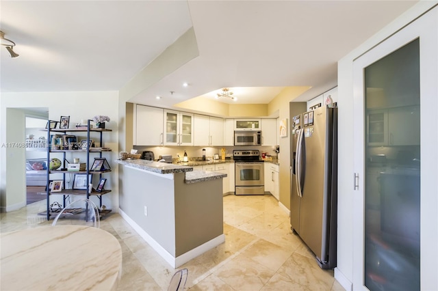 kitchen featuring appliances with stainless steel finishes, white cabinets, light stone counters, and kitchen peninsula