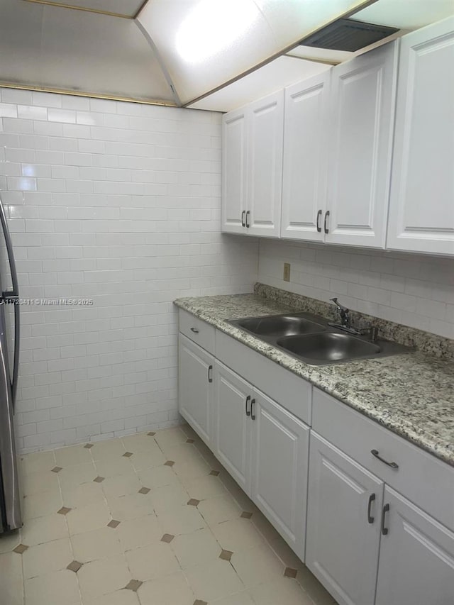 kitchen with white cabinetry, sink, light stone countertops, and tile walls