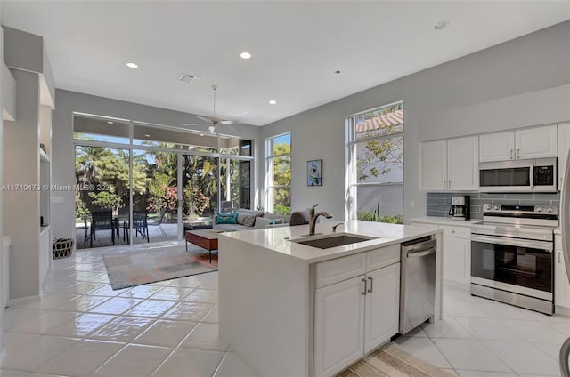 kitchen with sink, an island with sink, white cabinets, stainless steel appliances, and backsplash