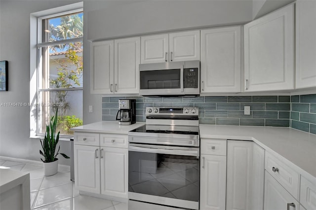 kitchen featuring appliances with stainless steel finishes, light tile patterned floors, white cabinets, and decorative backsplash