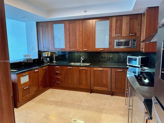 kitchen featuring sink, dark stone countertops, stainless steel microwave, black electric stovetop, and decorative backsplash