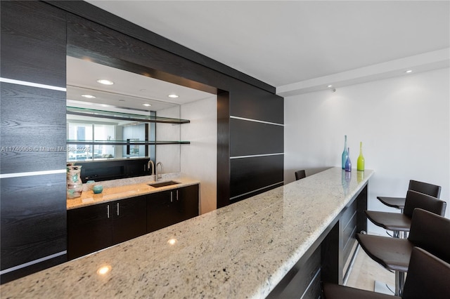 kitchen with dark cabinetry, light stone counters, and a sink