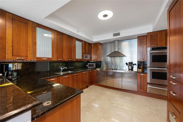 kitchen featuring a warming drawer, visible vents, appliances with stainless steel finishes, a sink, and wall chimney range hood