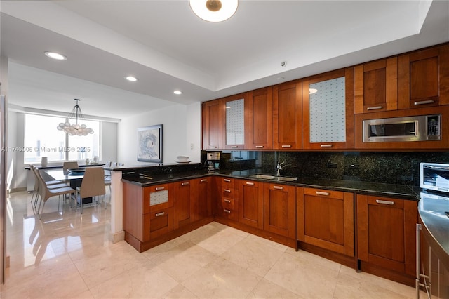 kitchen with stainless steel microwave, backsplash, glass insert cabinets, a sink, and a peninsula