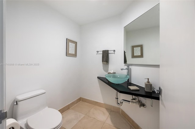 bathroom with tile patterned flooring, baseboards, a sink, and toilet