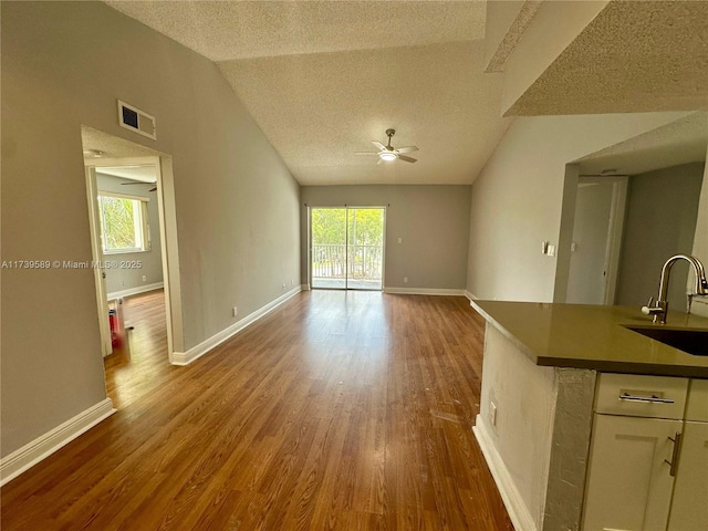 unfurnished living room with sink, ceiling fan, hardwood / wood-style floors, a textured ceiling, and vaulted ceiling