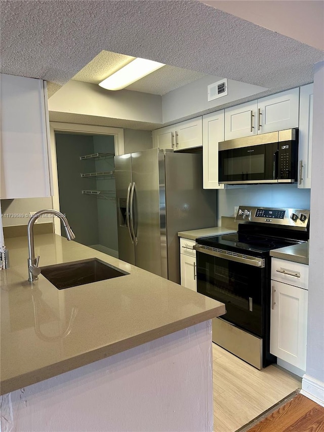 kitchen with sink, a textured ceiling, appliances with stainless steel finishes, light hardwood / wood-style floors, and white cabinets