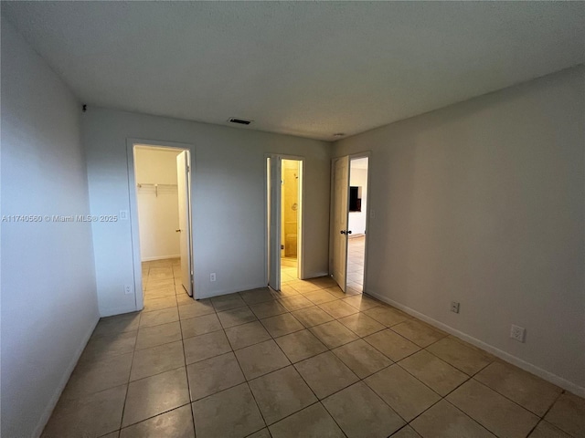 unfurnished bedroom featuring light tile patterned flooring, a walk in closet, and a closet