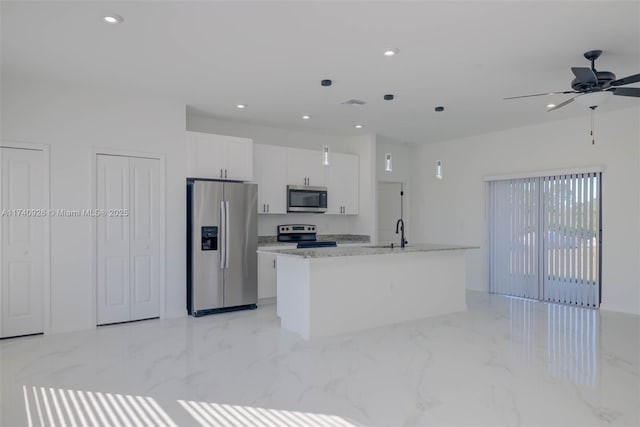 kitchen with appliances with stainless steel finishes, sink, white cabinets, light stone countertops, and a center island with sink