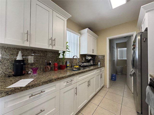 kitchen featuring sink, white cabinets, stainless steel refrigerator, and dark stone counters