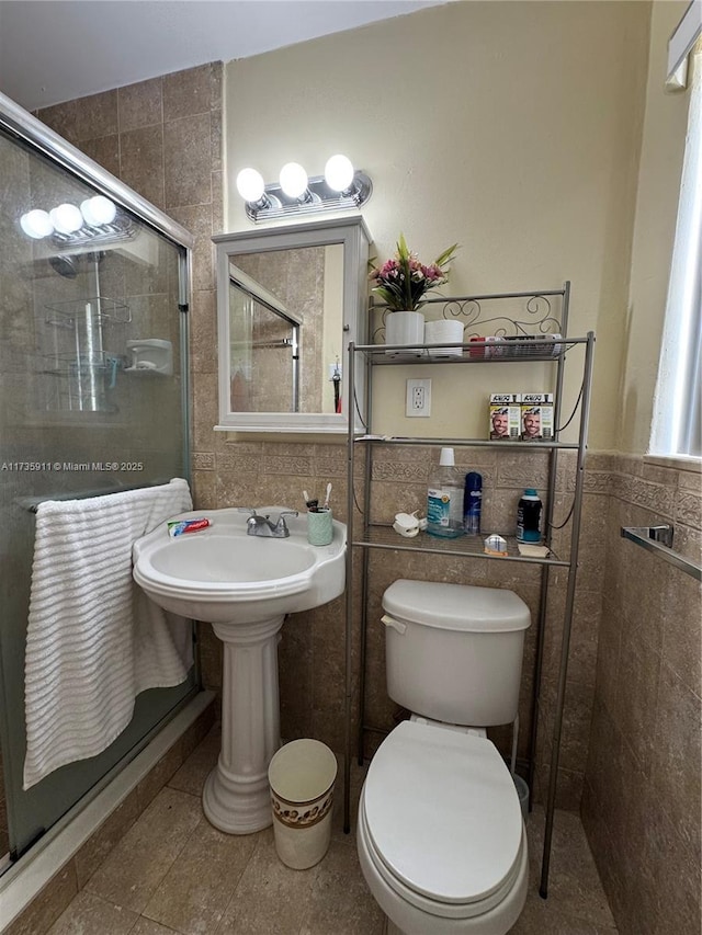 bathroom with toilet, an enclosed shower, sink, and tile walls