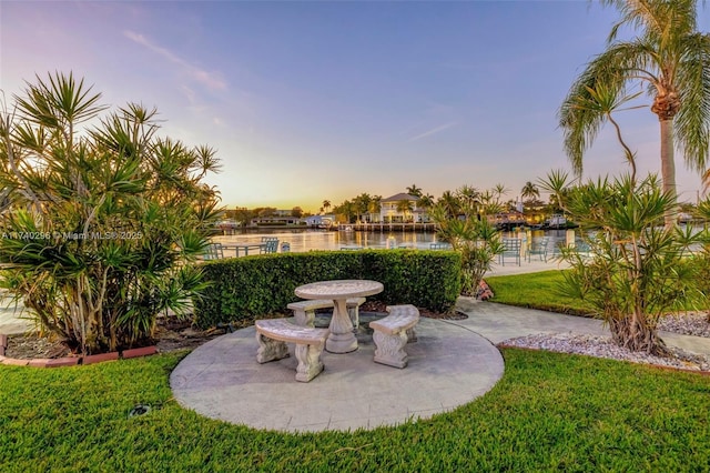 patio terrace at dusk featuring a yard and a water view