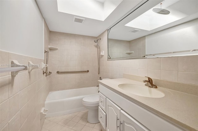 full bathroom featuring a skylight, tile walls, tiled shower / bath combo, vanity, and toilet