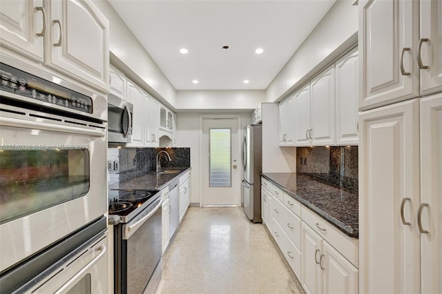 kitchen with dark stone countertops, stainless steel appliances, sink, and white cabinets