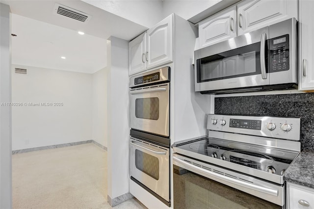 kitchen with white cabinetry, stainless steel appliances, dark stone countertops, and backsplash