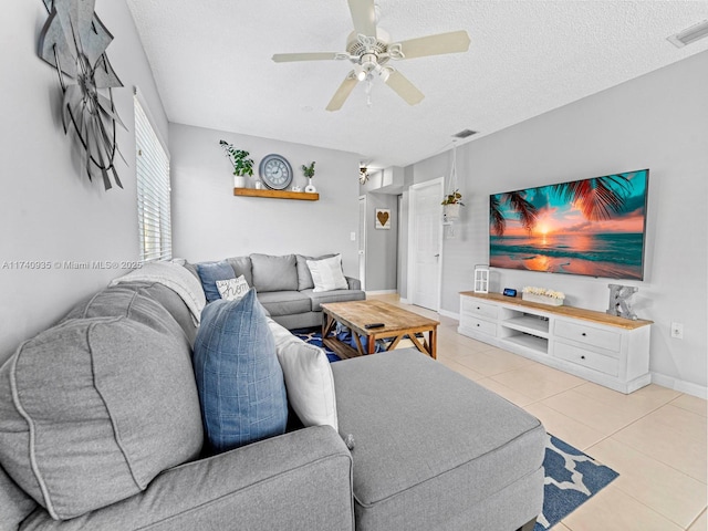 living room featuring baseboards, light tile patterned floors, a textured ceiling, visible vents, and ceiling fan