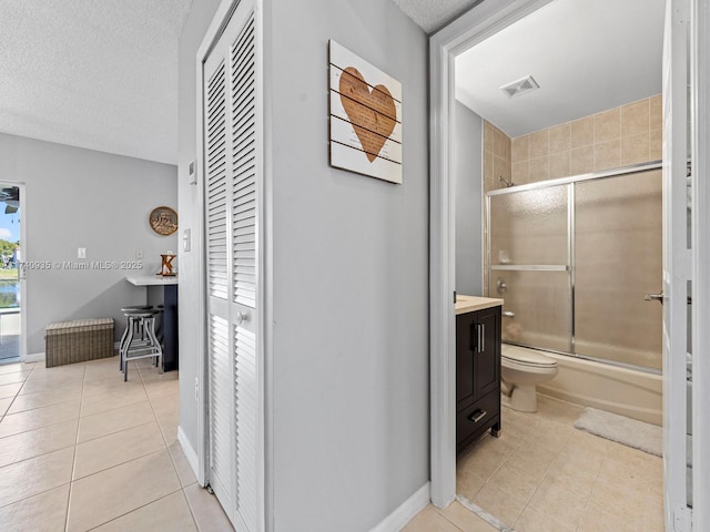 full bathroom featuring bath / shower combo with glass door, vanity, toilet, tile patterned floors, and a textured ceiling