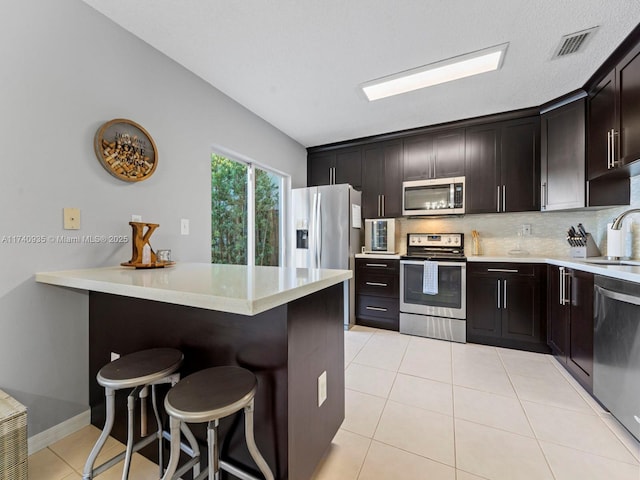 kitchen with a kitchen bar, sink, light tile patterned floors, kitchen peninsula, and stainless steel appliances