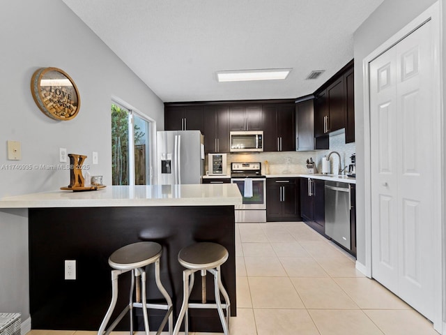 kitchen with a breakfast bar, a peninsula, light tile patterned floors, visible vents, and stainless steel appliances