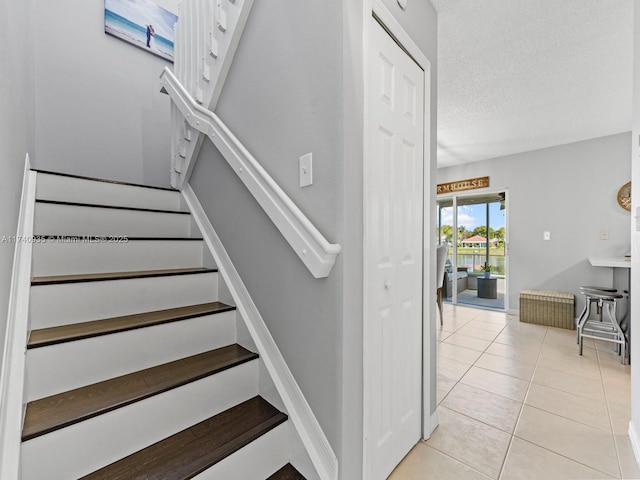 stairs with tile patterned floors, baseboards, and a textured ceiling