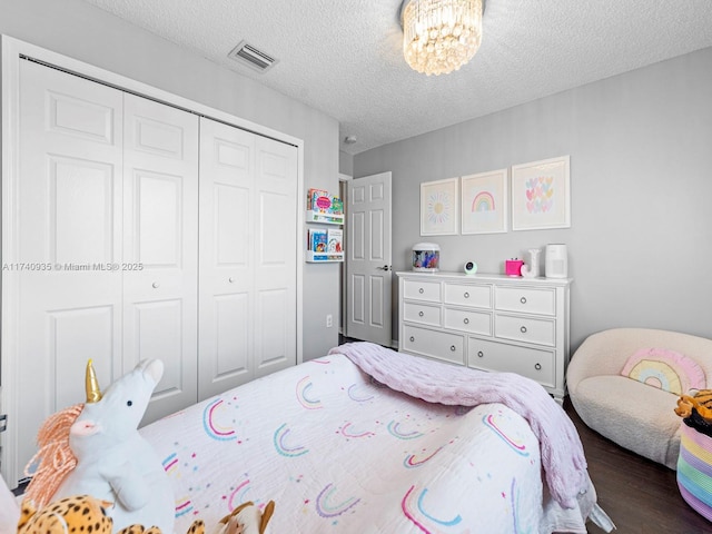 bedroom featuring a closet, an inviting chandelier, a textured ceiling, visible vents, and dark wood finished floors