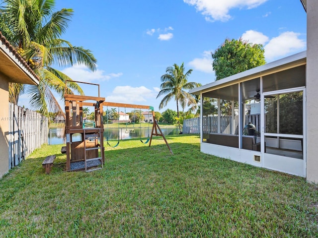 view of yard featuring a water view, ceiling fan, a playground, and a sunroom