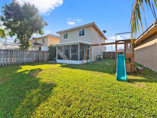 back of house featuring a sunroom, a fenced backyard, stucco siding, a lawn, and a playground