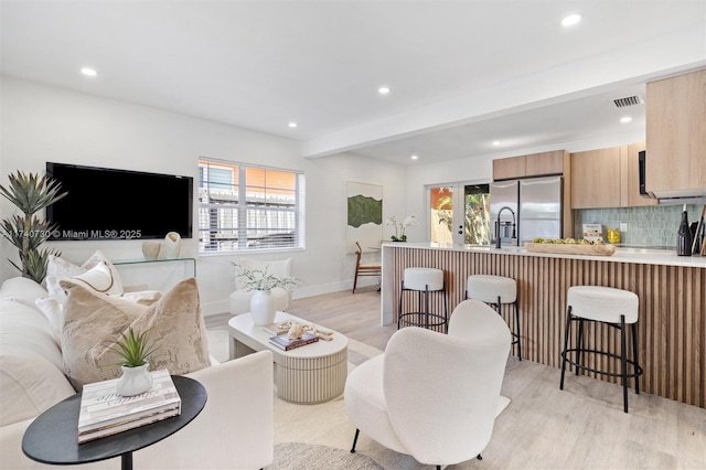 living room featuring beam ceiling, sink, and light hardwood / wood-style flooring