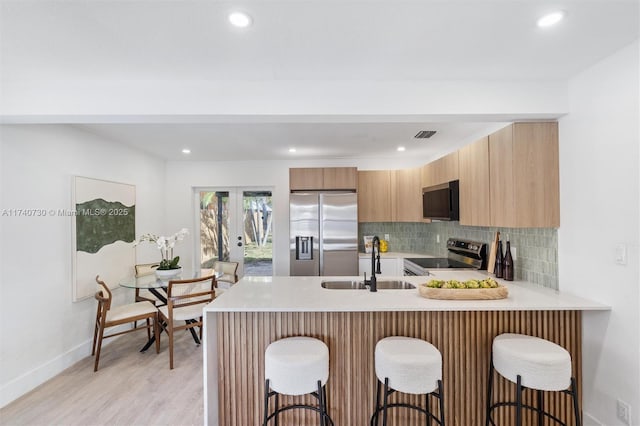 kitchen featuring sink, tasteful backsplash, kitchen peninsula, stainless steel appliances, and light hardwood / wood-style floors