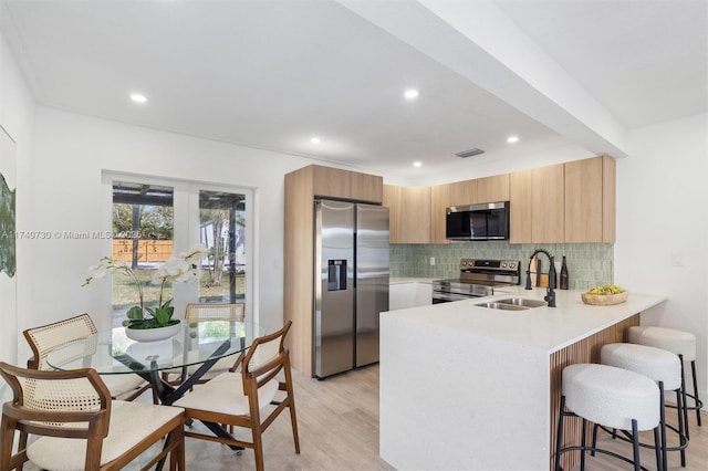 kitchen with appliances with stainless steel finishes, tasteful backsplash, sink, light hardwood / wood-style floors, and kitchen peninsula