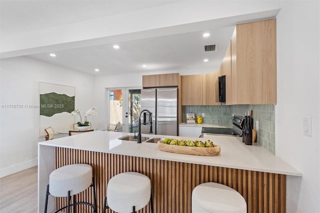 kitchen featuring sink, stainless steel fridge, electric range oven, a kitchen bar, and kitchen peninsula