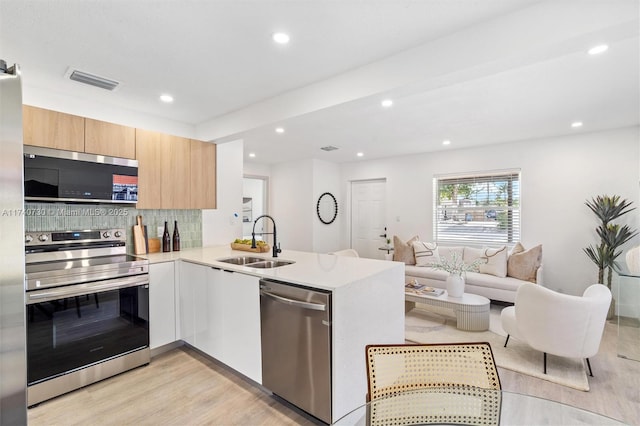 kitchen featuring sink, tasteful backsplash, light wood-type flooring, appliances with stainless steel finishes, and kitchen peninsula