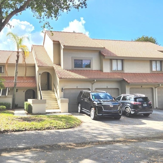 townhome / multi-family property featuring driveway, a tiled roof, an attached garage, and stucco siding